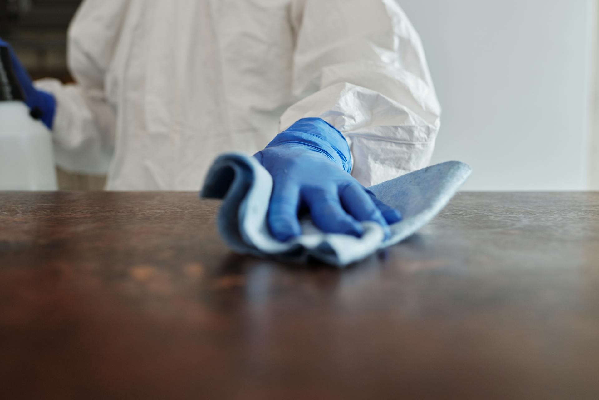 A gloved hand cleaning a furniture surface with a blue cloth.